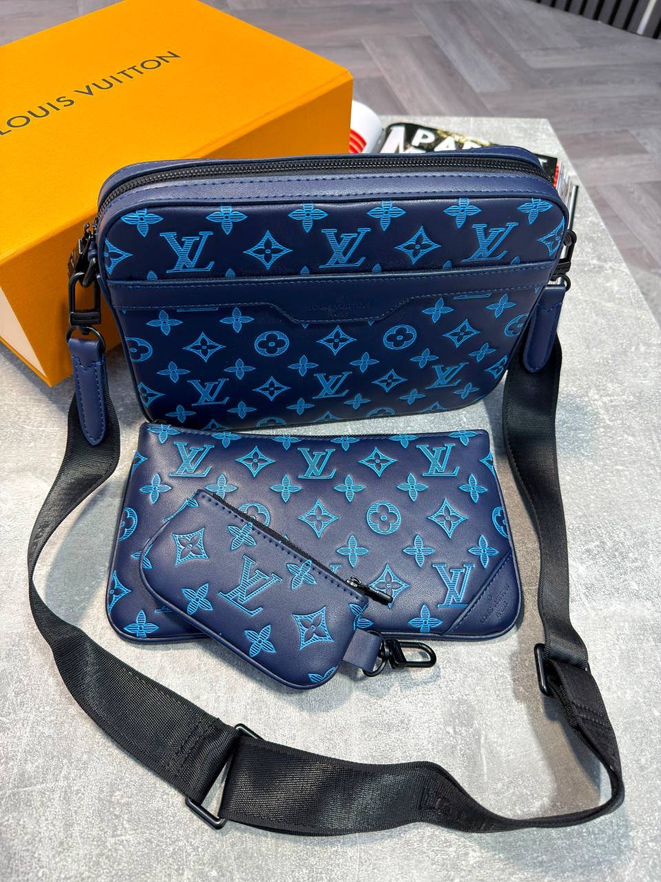 Louis Vuitton monogram shoulder bag set in navy blue, including a larger top flap bag and a smaller envelope-style pouch, displayed with a black shoulder strap on a gray surface next to an orange Louis Vuitton box.