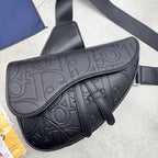A black pebbled leather shoulder bag with an embossed monogram pattern, shown on a light gray concrete floor with its strap extending out of frame.