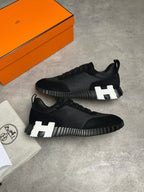 Black sneakers with a logo next to an orange box on a gray surface