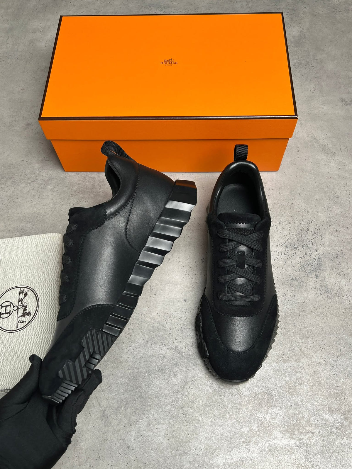 Black sneakers with orange box on a gray surface