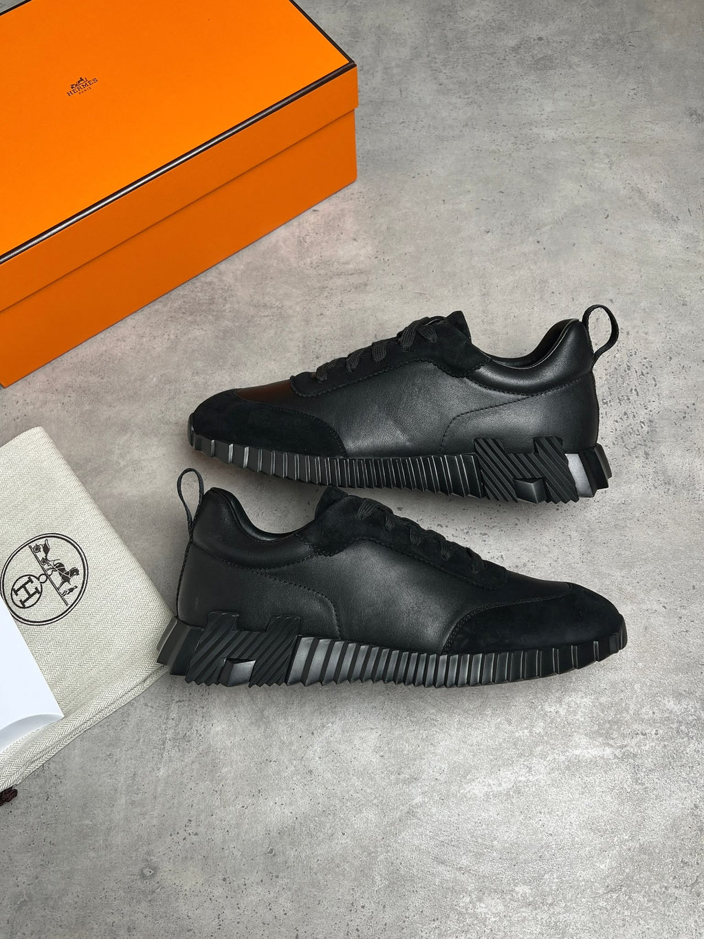Black sneakers on a gray surface with an orange box and white paper in the background.