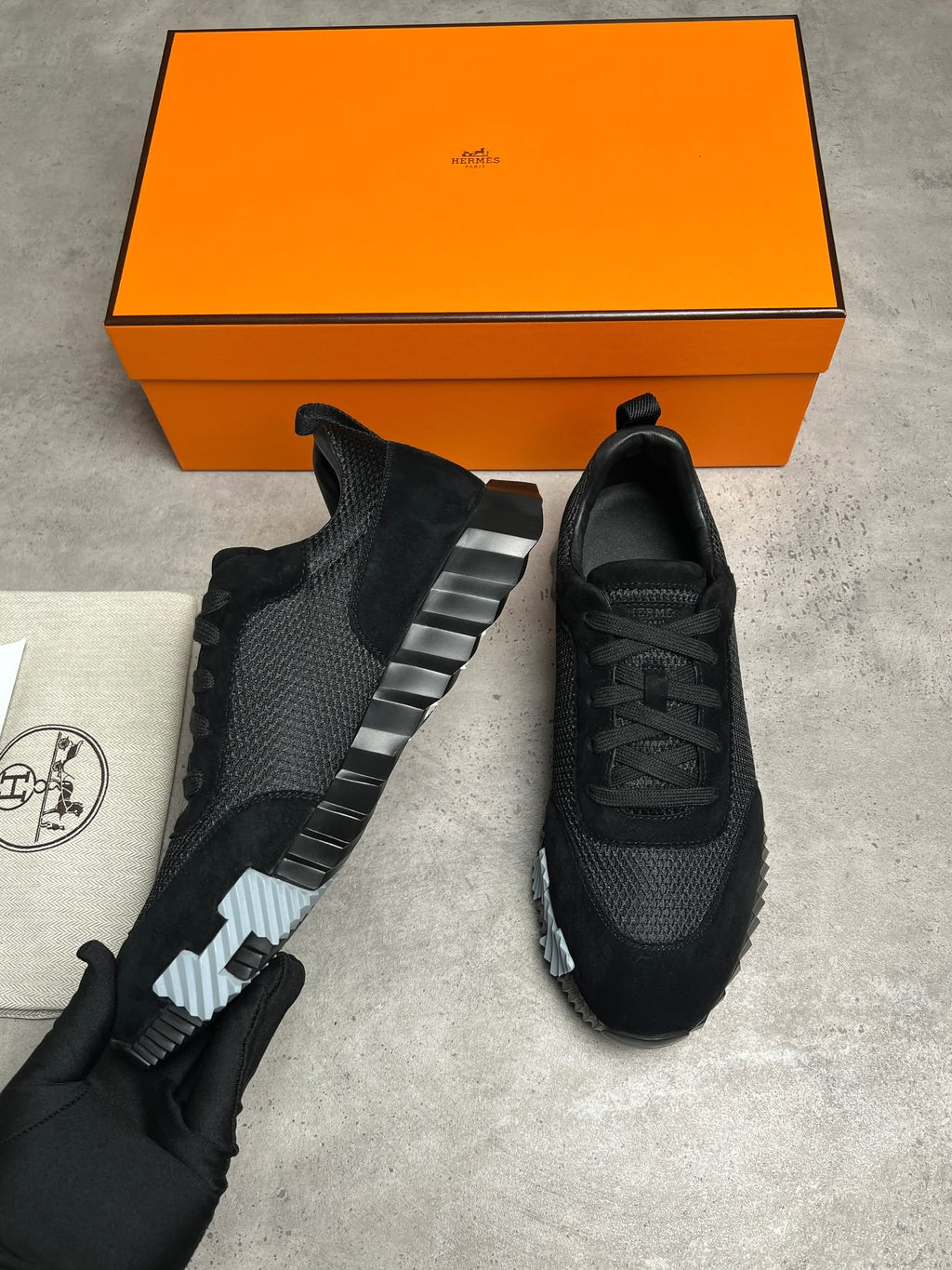 Black sneakers with a silver stripe on a gray surface next to an orange box.