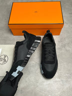 Black sneakers with a silver stripe on a gray surface next to an orange box.
