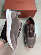 A pair of taupe-brown and gray mesh sneakers with white midsoles, shown with a brown shoebox branded Love Brand in the background.