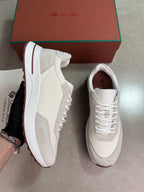 A pair of beige and white platform sneakers with a brown sole, shown next to their brown and green branded box. One shoe is held up by a hand, and the other lies flat on a gray floor.