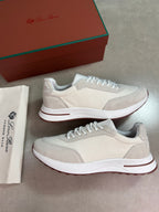 A pair of beige and white sneakers with white laces, displayed next to their brown and green branded shoebox and a white dust bag on a gray floor.