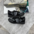 A pair of black and gray camouflage low-top sneakers displayed on a gray stone surface, with a matching camouflage shoebox and printed inserts behind them.