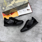 Black sneakers on a concrete surface with a camouflage shoe box in the background.