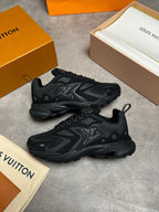 A pair of black Louis Vuitton sneakers displayed on a gray concrete surface, surrounded by orange and beige Louis Vuitton packaging boxes and dust bags.