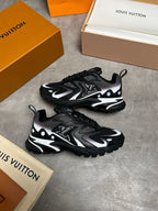 A pair of Louis Vuitton low-top sneakers in black, gray, and white, styled with branded orange and beige shoeboxes on a gray concrete floor.