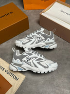 A pair of Louis Vuitton chunky sneakers in white and gray, displayed on a gray concrete surface with Louis Vuitton boxes and dust bags around them.