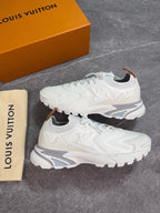 A pair of white Louis Vuitton low-top sneakers displayed on a gray stone-textured surface, with the orange Louis Vuitton shoebox and a beige dust bag visible in the background.
