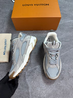 A pair of Louis Vuitton chunky sneakers in light gray and white mesh with beige accents, shown next to their orange Louis Vuitton box and dust bag on a gray floor.