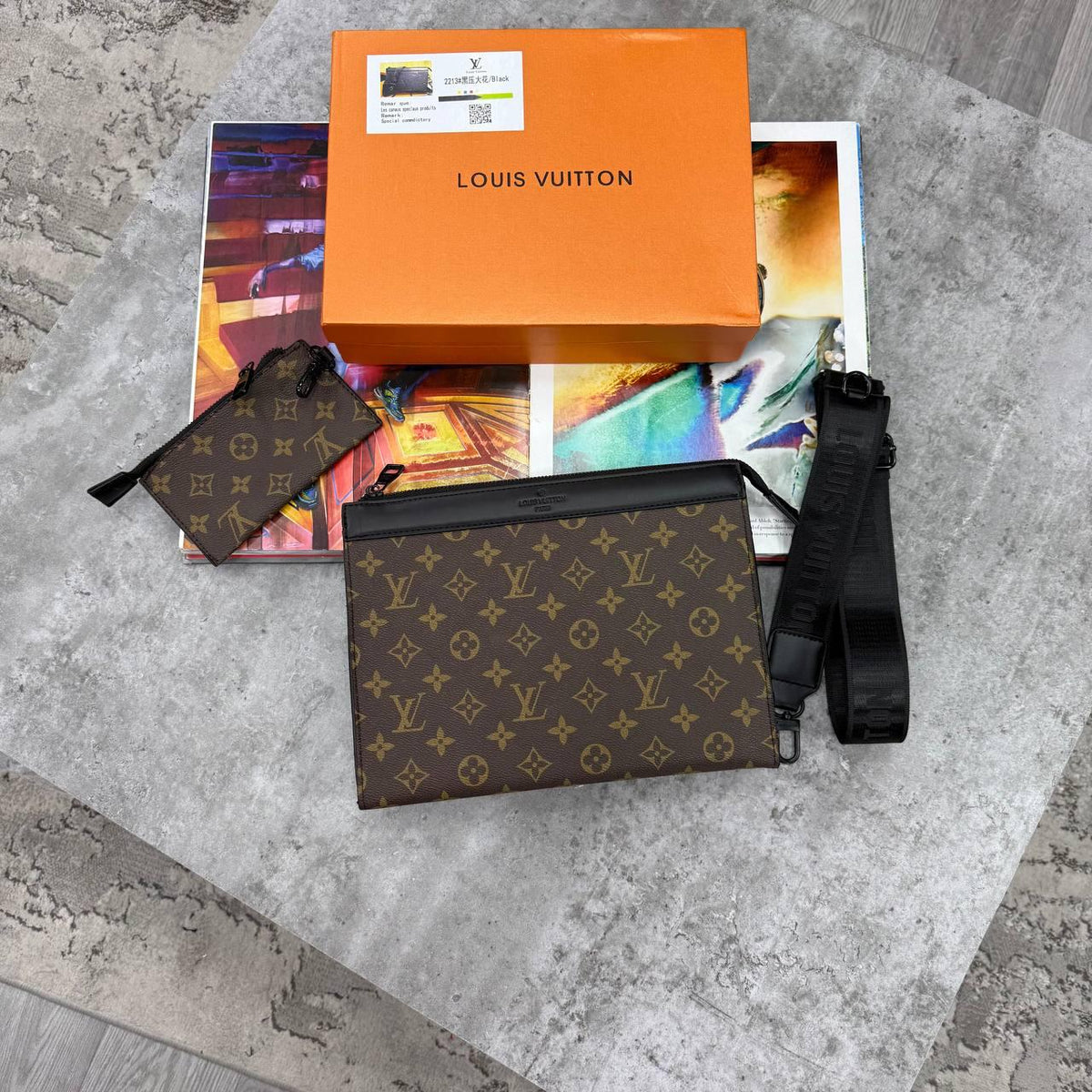 Louis Vuitton monogram pouch with a black shoulder strap, shown with an orange Louis Vuitton box, hangtag, and colorful magazine on a gray stone surface.